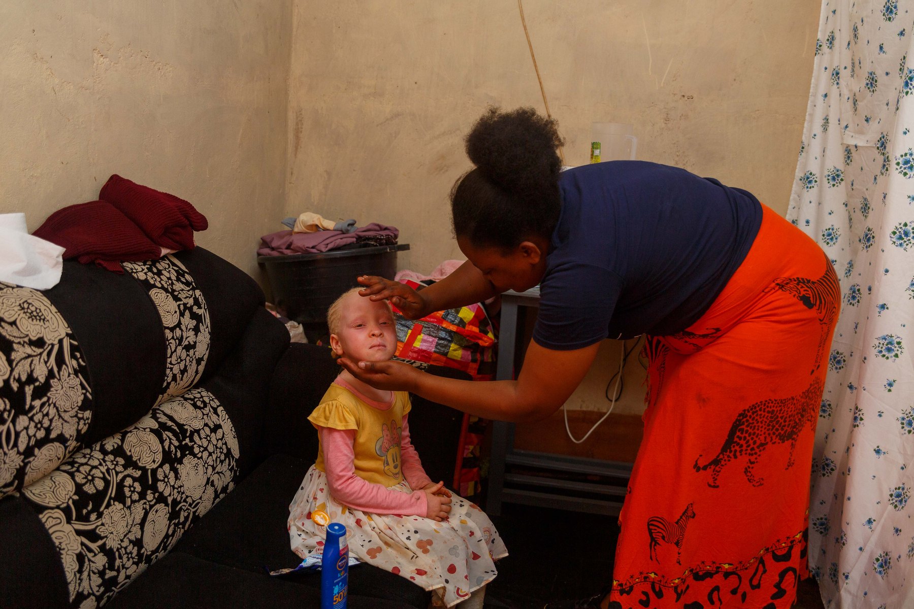 A health worker sitting with a young child with albinism and her family at home.