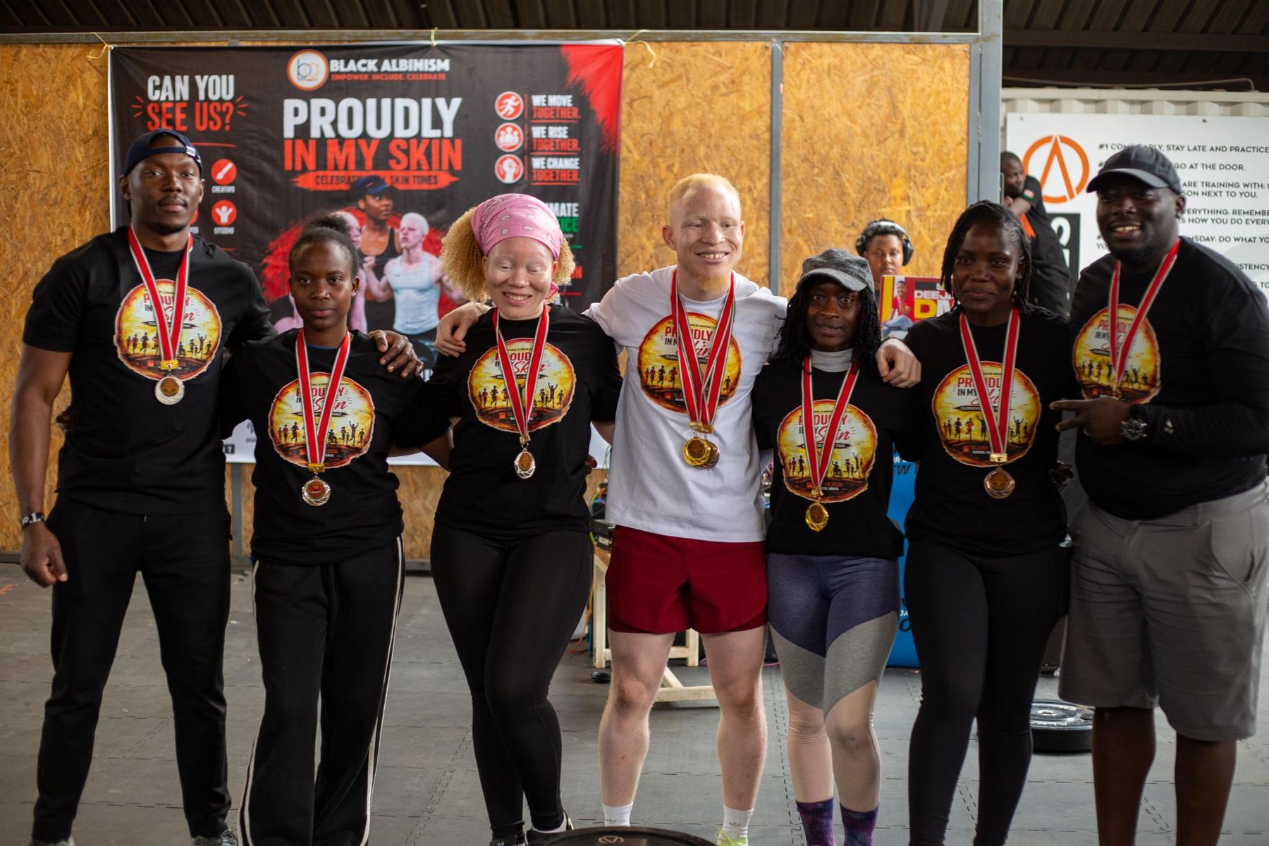 Members of Black Albinism with medals after a sports day, in front of a banner reading Proudly In My Skin.